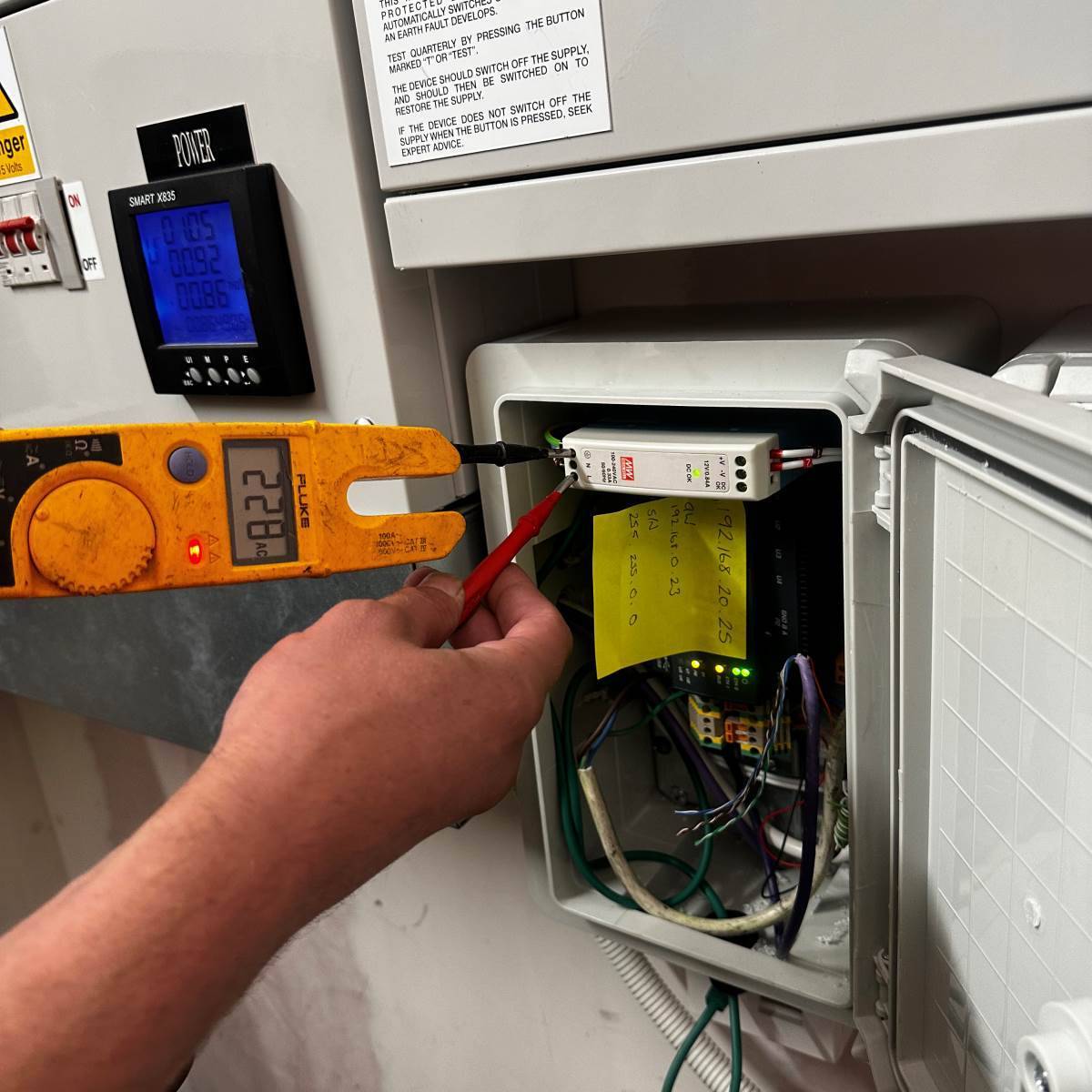 Fluke clamp meter taking a live current reading at a commercial control panel during commissioning