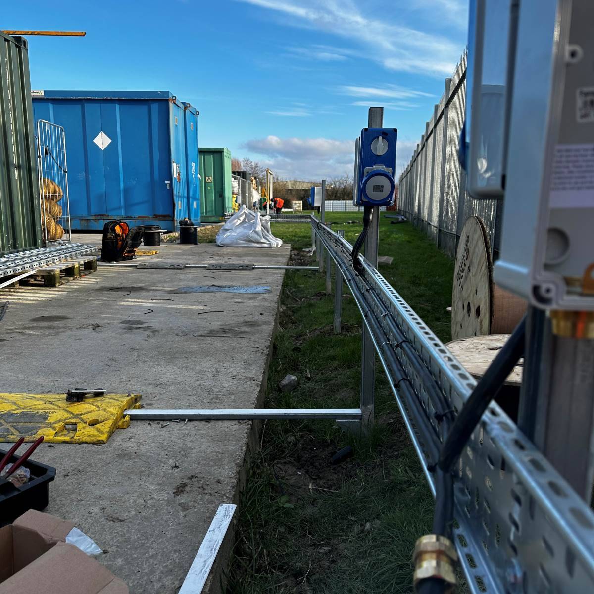Galvanised cable tray and containment run along a commercial site fence supplying a three-phase distribution point
