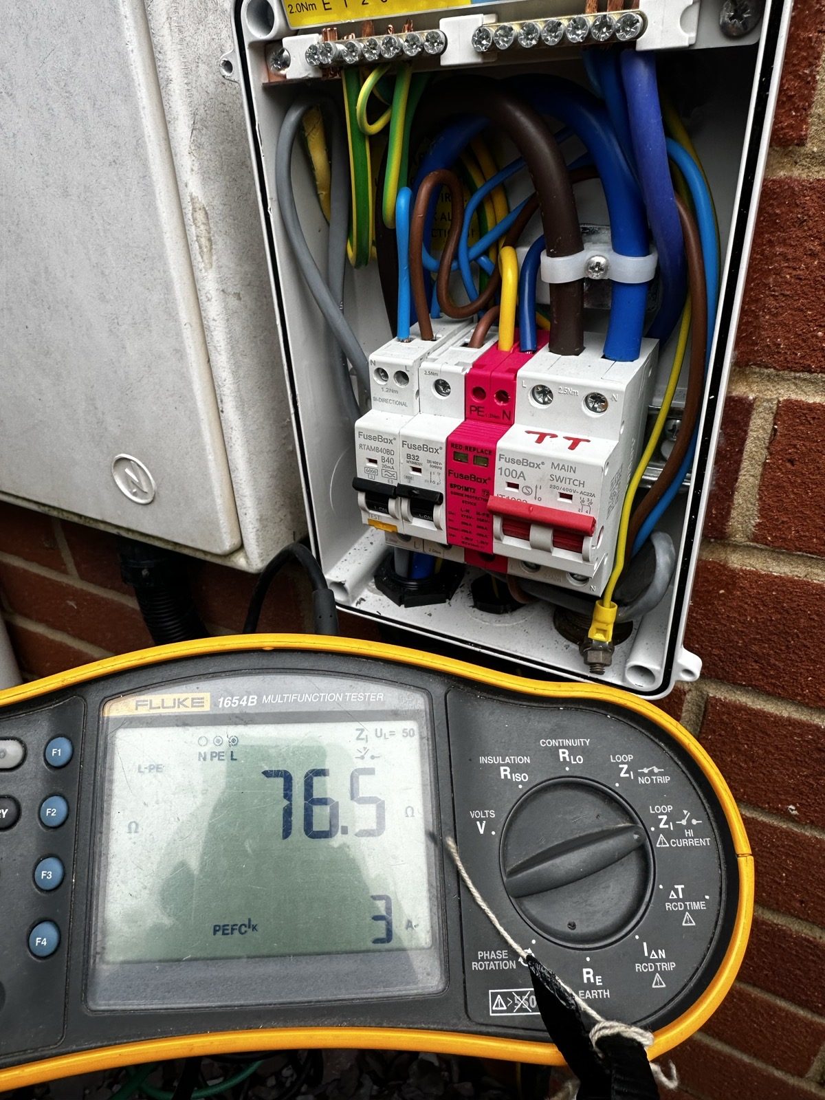 Fluke 1654B multifunction tester reading 76.5 ohm at an outdoor TT consumer unit during an EICR