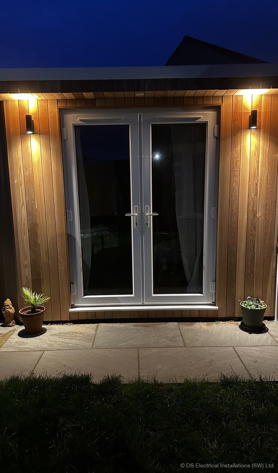 Garden room with warm wall lights on cedar cladding at dusk