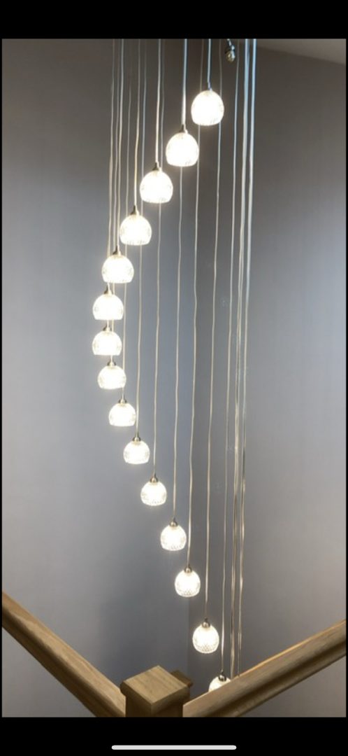 Cascade of glass pendant lights falling through a double-height oak stairwell, installed by DS Electrical